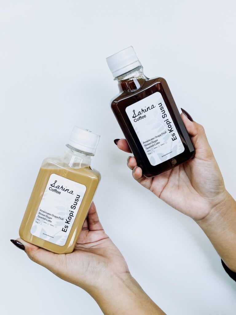 Hands holding two bottles of coffee.